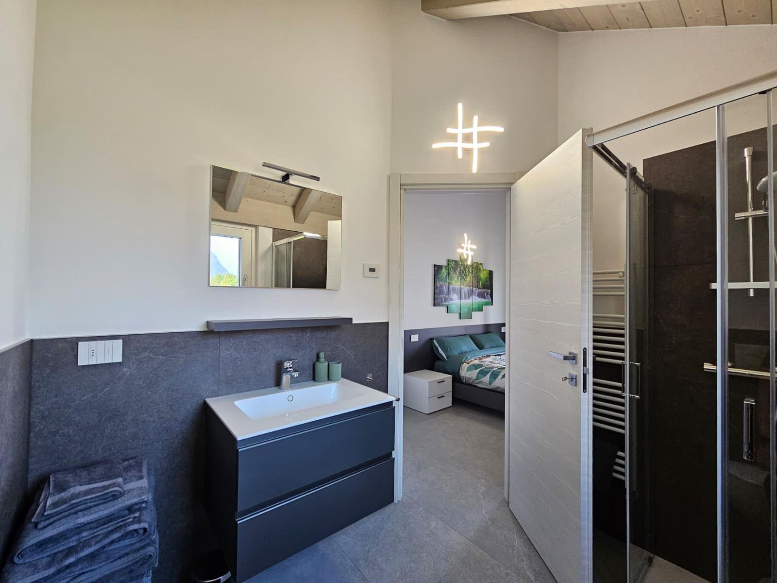 Badezimmer mit Dusche und Waschbecken. Blick in Schlafzimmer mit Bett und Wandbild.