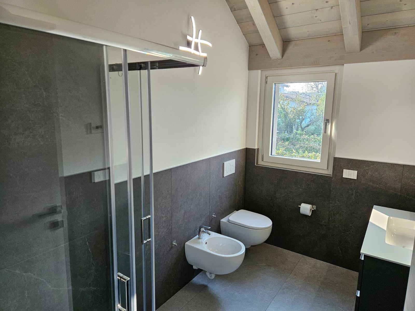 Badezimmer mit Dusche, Toilette und Waschbecken. Holzdecke und Fenster mit Blick.