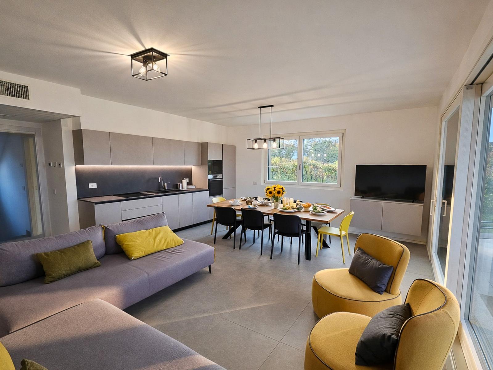 Wohn- und Essbereich mit Küche, Sofa, Stühlen und Fernseher.