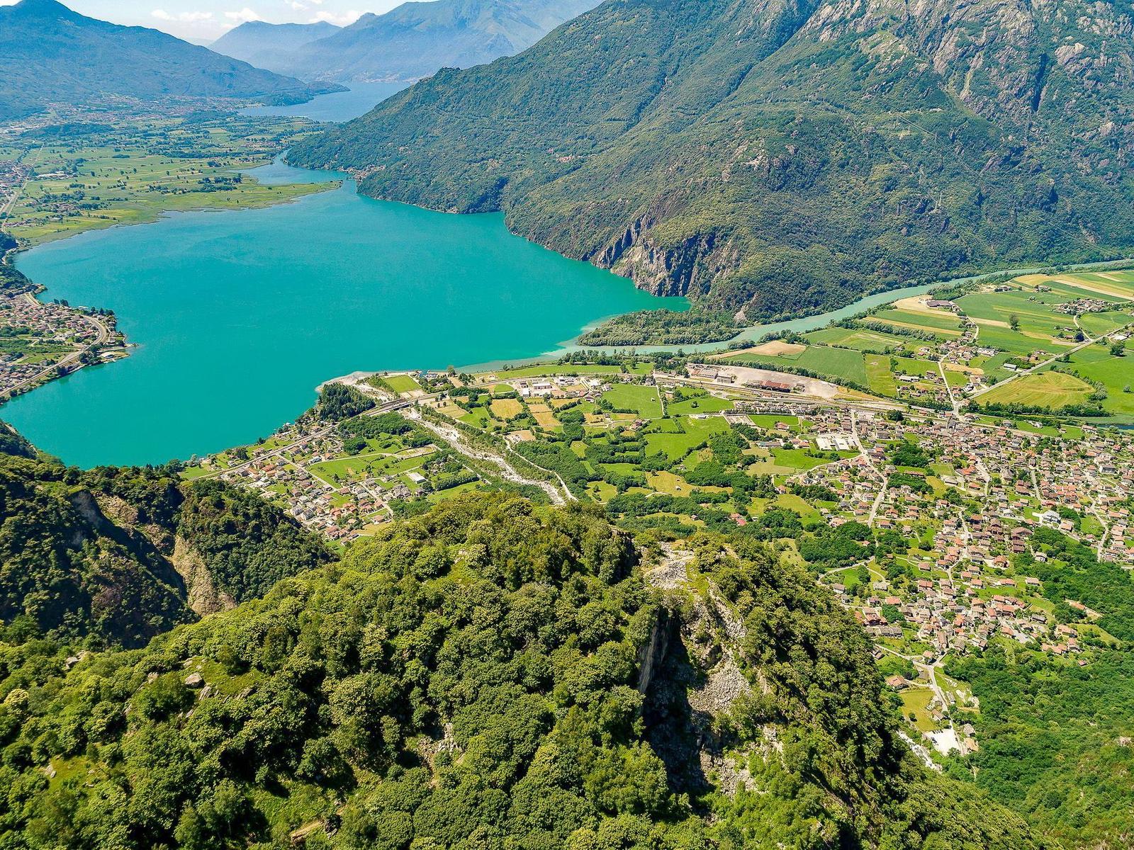 Luftbild eines Sees zwischen grünen Bergen und kleinen Dörfern.