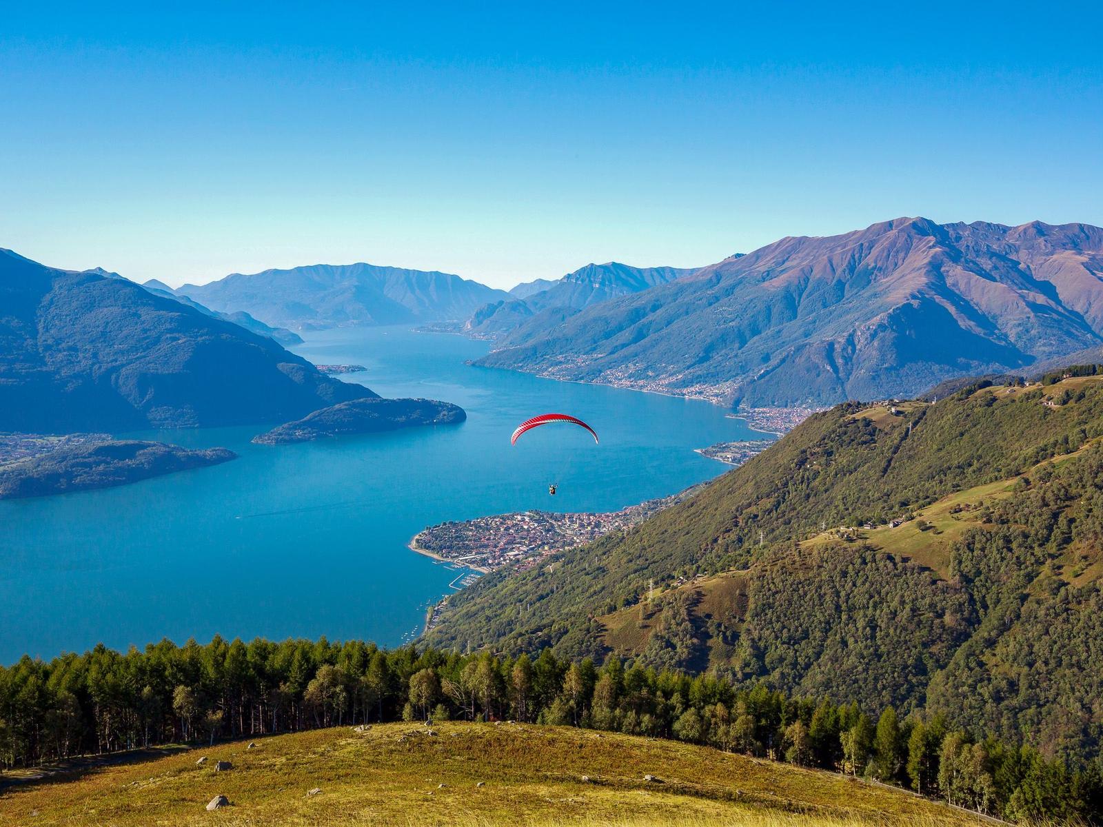 Paragleiter fliegt über einen See zwischen Bergen.