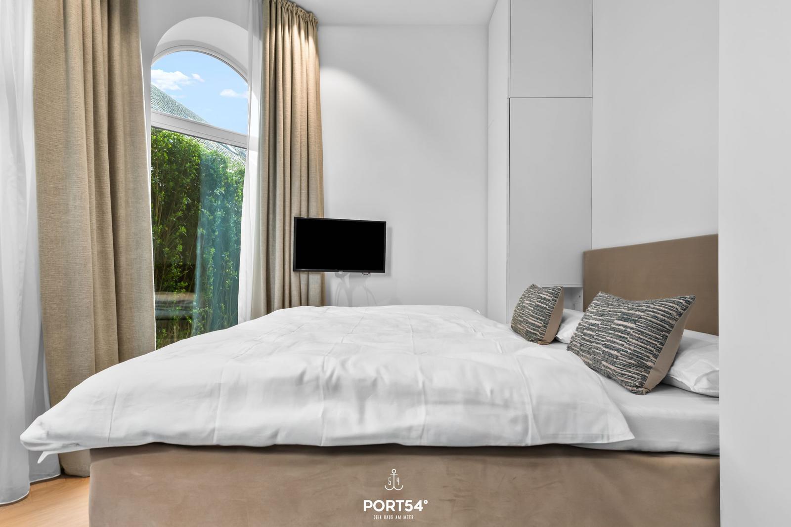 Schlafzimmer mit Bett, TV und Bogenfenster mit Blick auf Grün