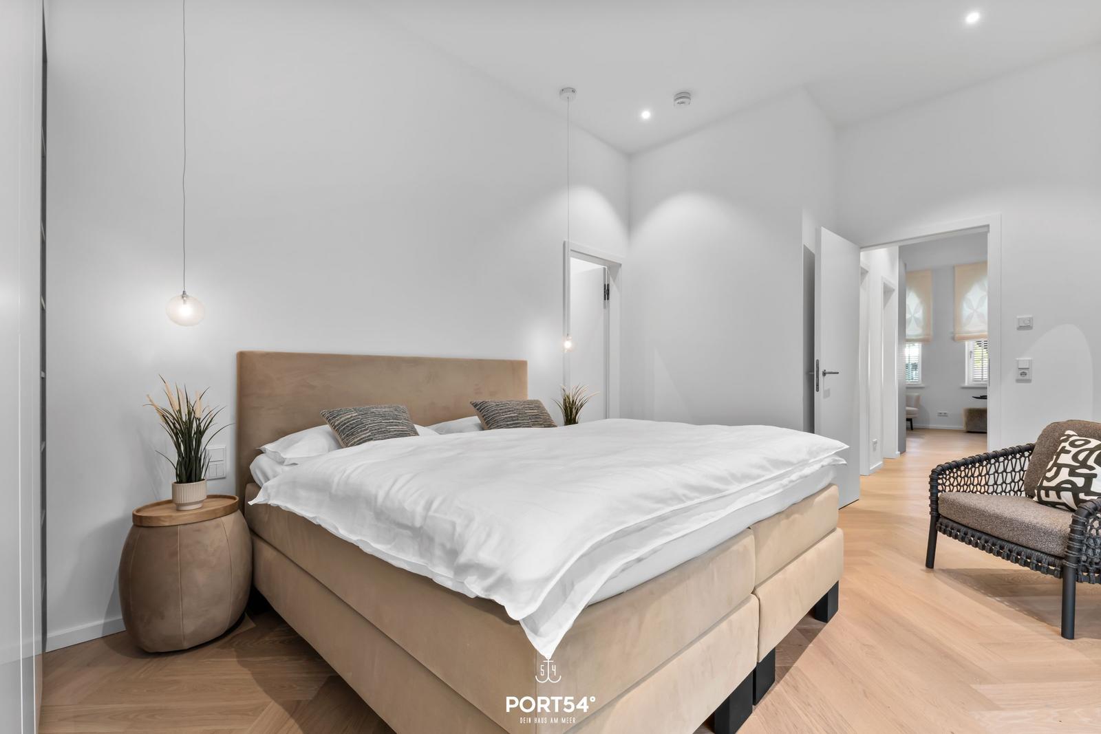 Schlafzimmer mit Bett, Nachttisch und Sessel. Holzboden und helle Wände.