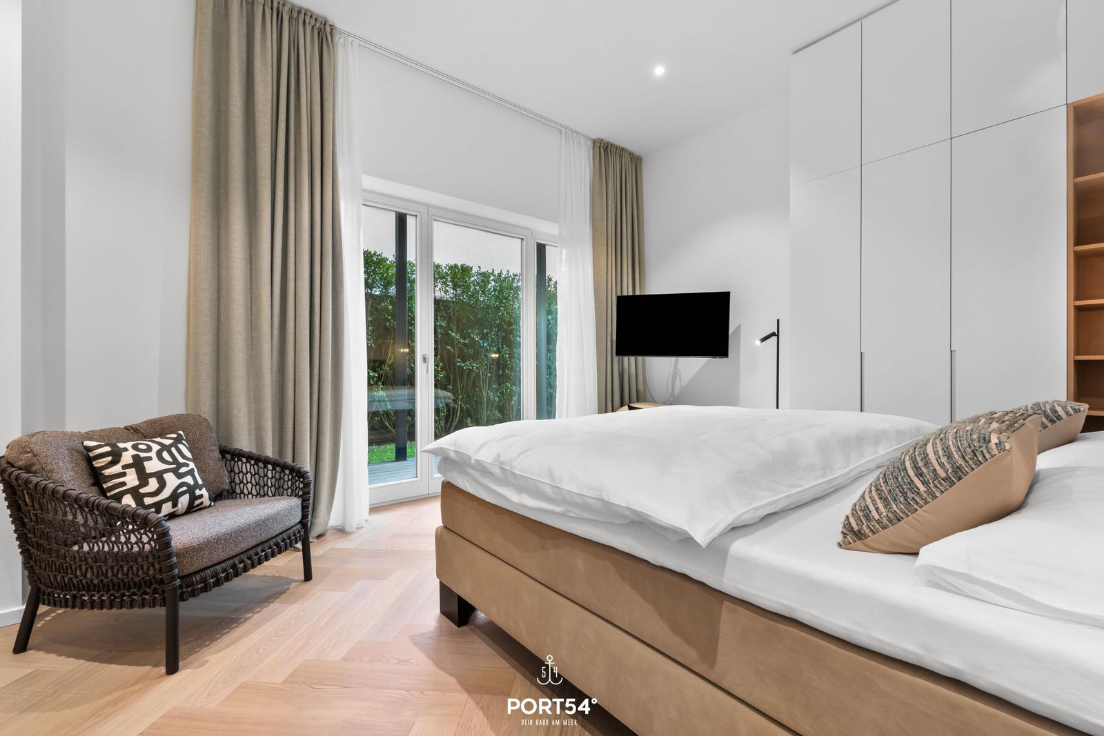 Schlafzimmer mit Bett, Sessel und Blick auf Garten.