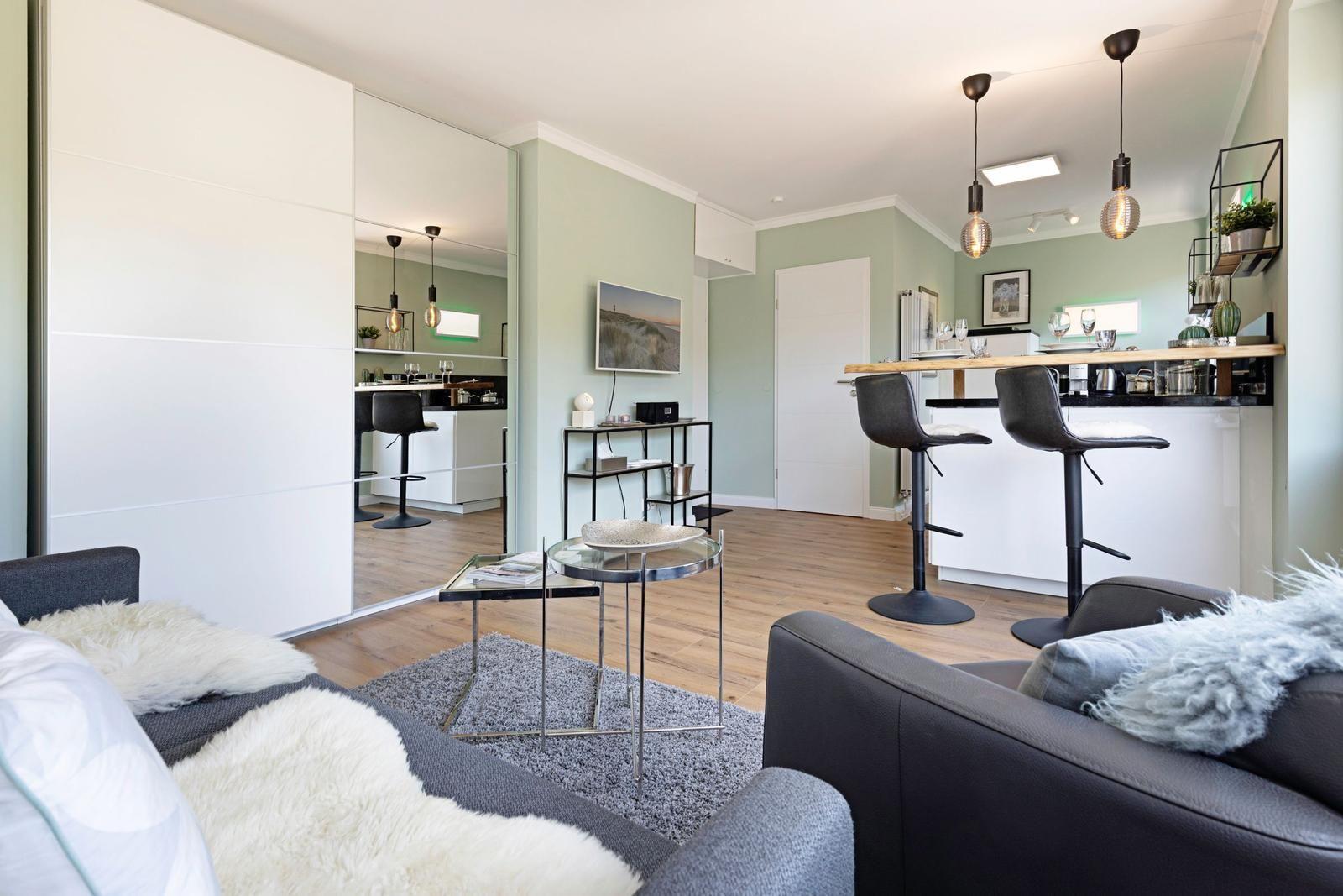 Wohnbereich mit Sofa, Couchtisch und Barhocker. Spiegelwand und Holzboden sichtbar.