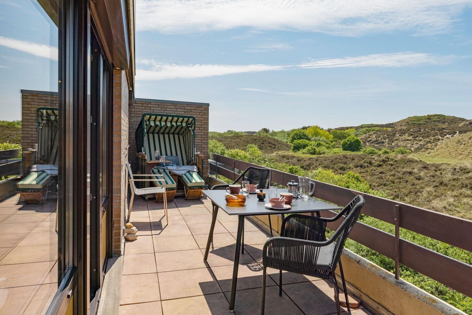 Terrasse mit Tisch, Stühlen und Blick auf grüne Hügel.