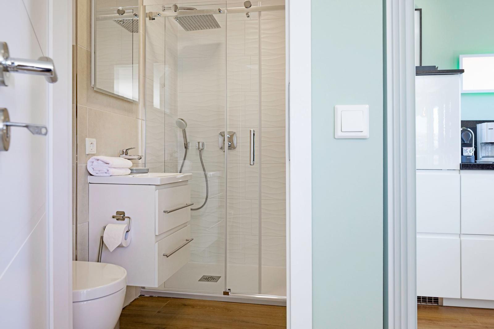 Badezimmer mit Dusche, Waschbecken und Toilette. Holzfußboden und helle Wände.