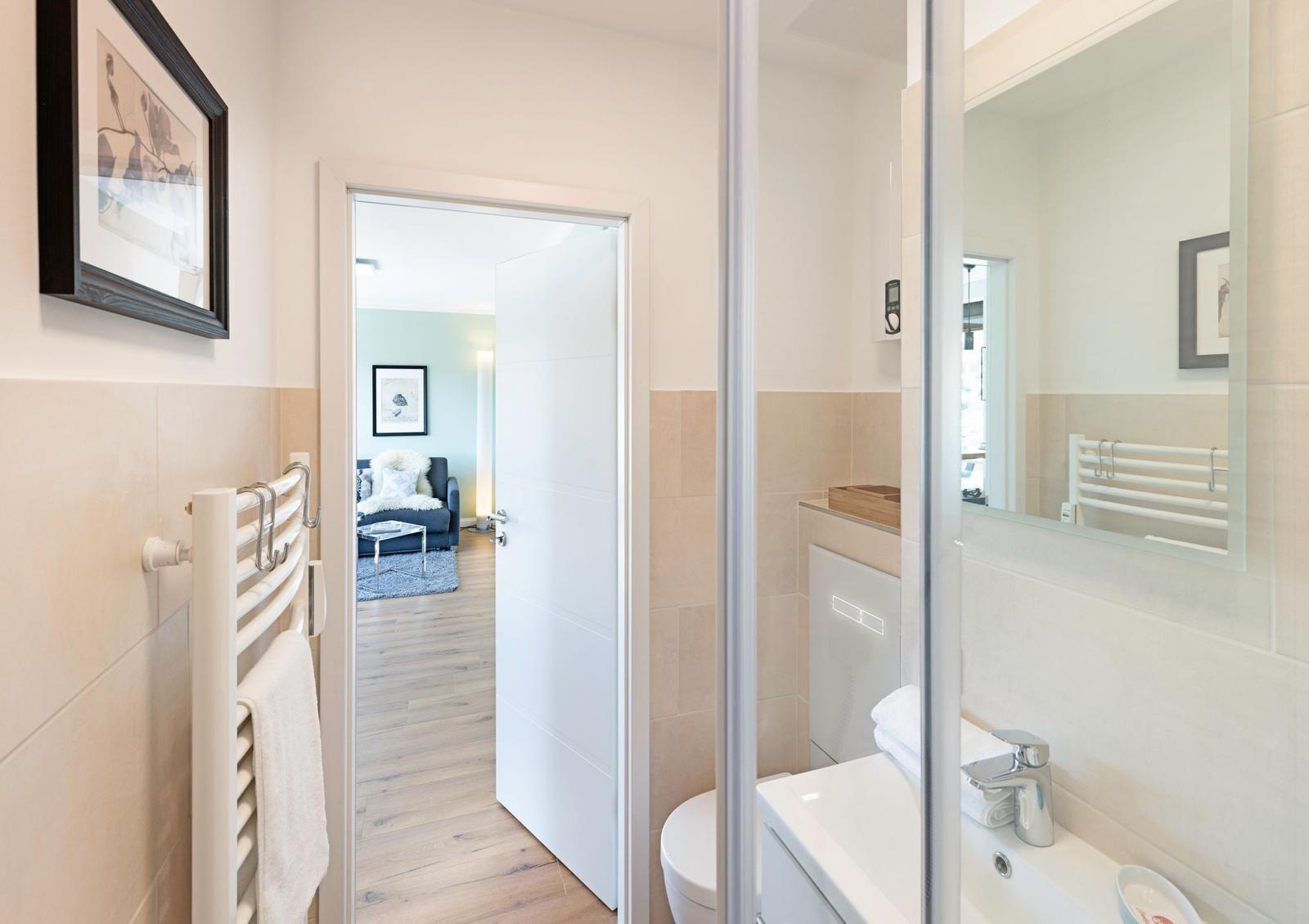 Badezimmer mit Dusche, Waschbecken und Heizkörper. Durchgang zur Wohnfläche mit Sofa.