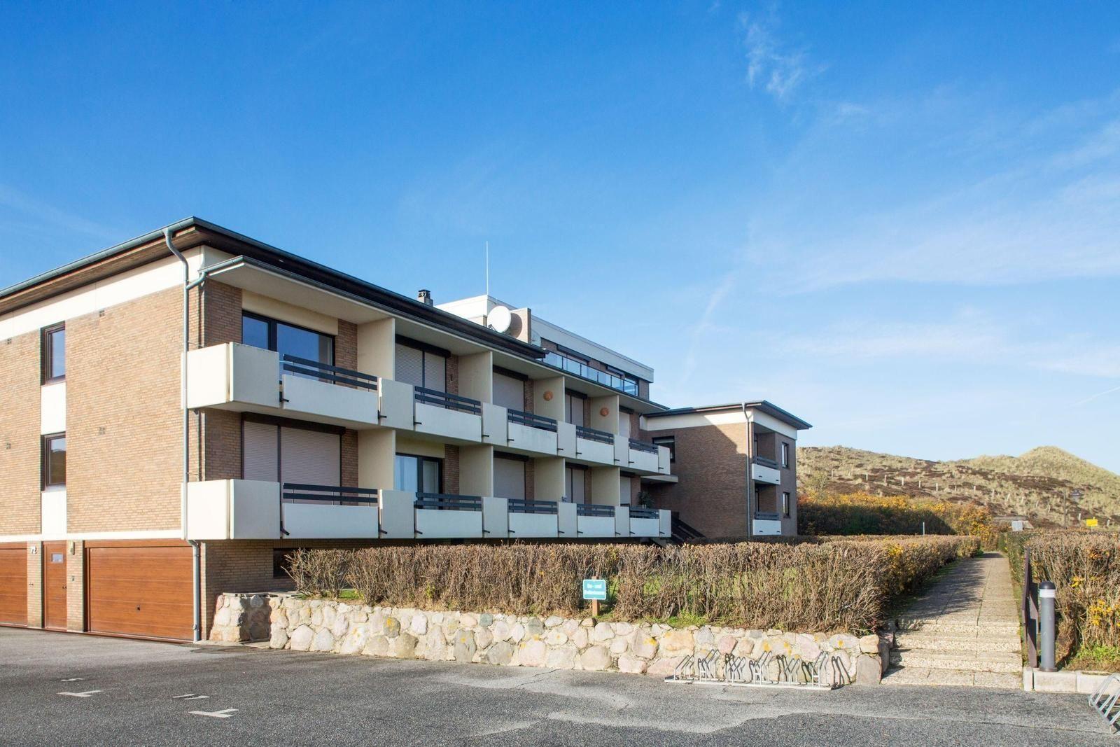 Modernes Mehrfamilienhaus mit Balkonen und Garage. Hintergrund: Hügel mit trockenem Buschwerk.