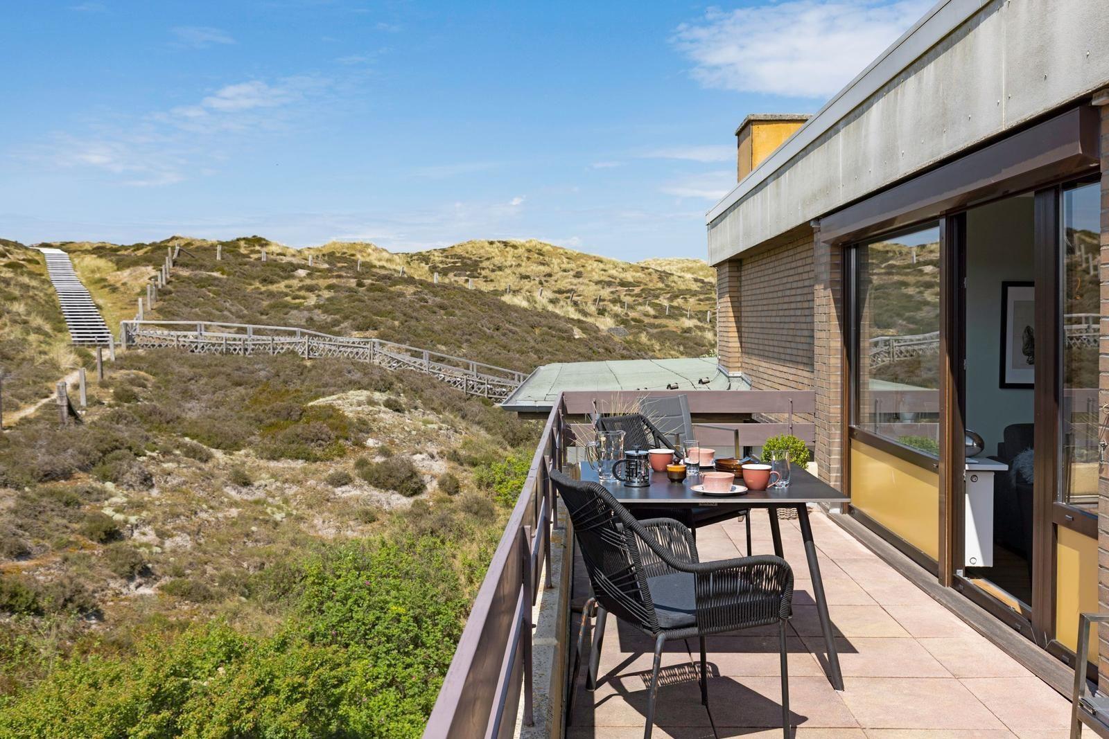Terrasse mit Tisch und Stühlen, Blick auf Dünenlandschaft.
