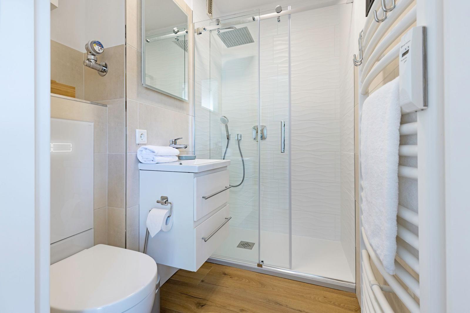 Bad mit Dusche, Waschbecken und Toilette. Holzfußboden und Heizung.