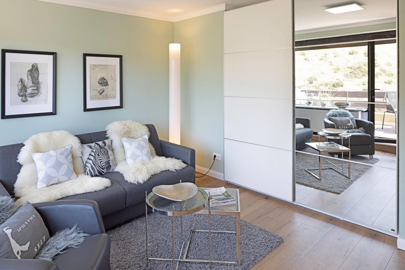 Wohnzimmer mit Sofa, Teppich und Glas-Tisch. Durchgehende Glastür führt auf Balkon.