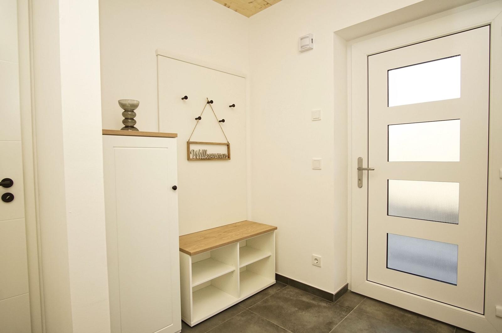 Eingangsbereich mit weißen Wänden, Holzbank und Tür mit Glasfeldern.