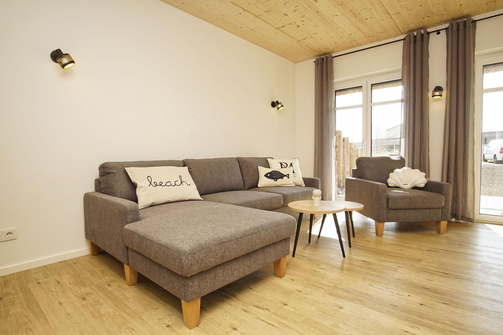 Wohnzimmer mit Sofa, Sessel und Holzboden. Fenster mit Vorhängen.