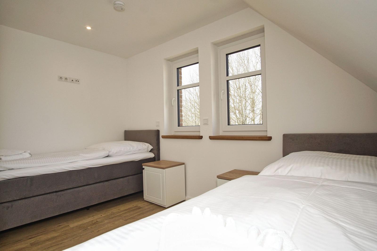 Zwei Betten mit weißen Laken und Holzboden. Zwei Fenster mit Blick nach draußen.