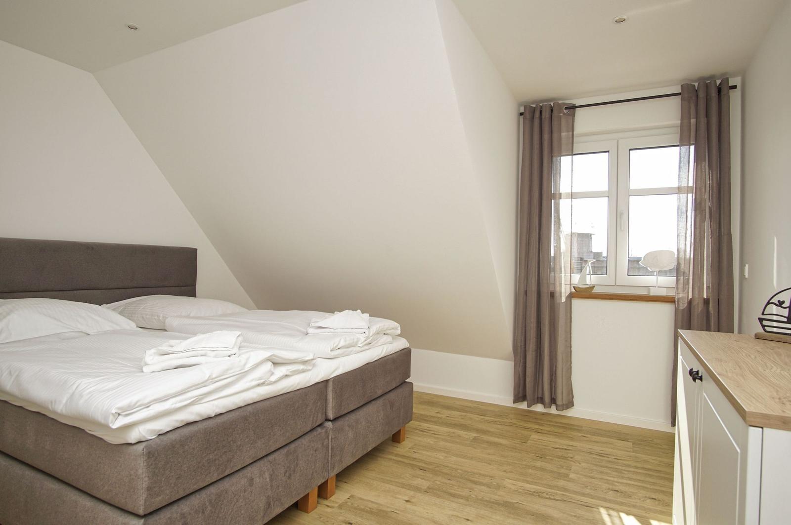 Schlafzimmer mit Doppelbett, Holzboden und Fenster mit Vorhängen.
