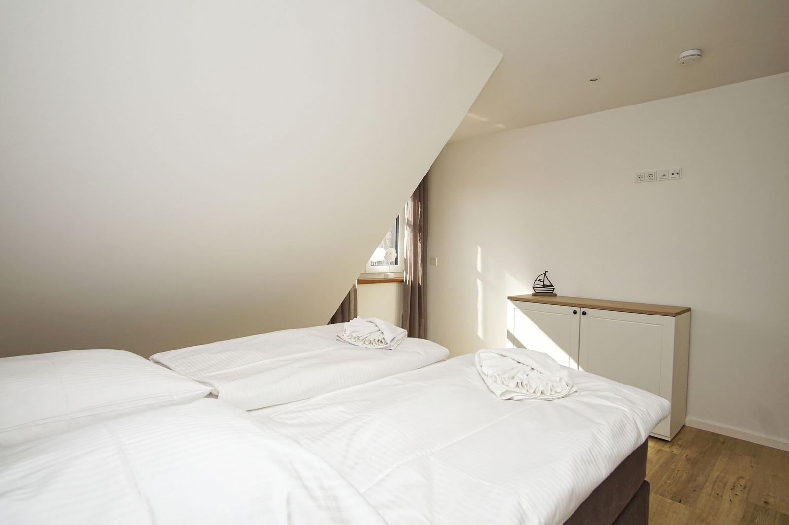 Schlafzimmer mit Doppelbett, Schrank und Fenster unter Dachschrägen.