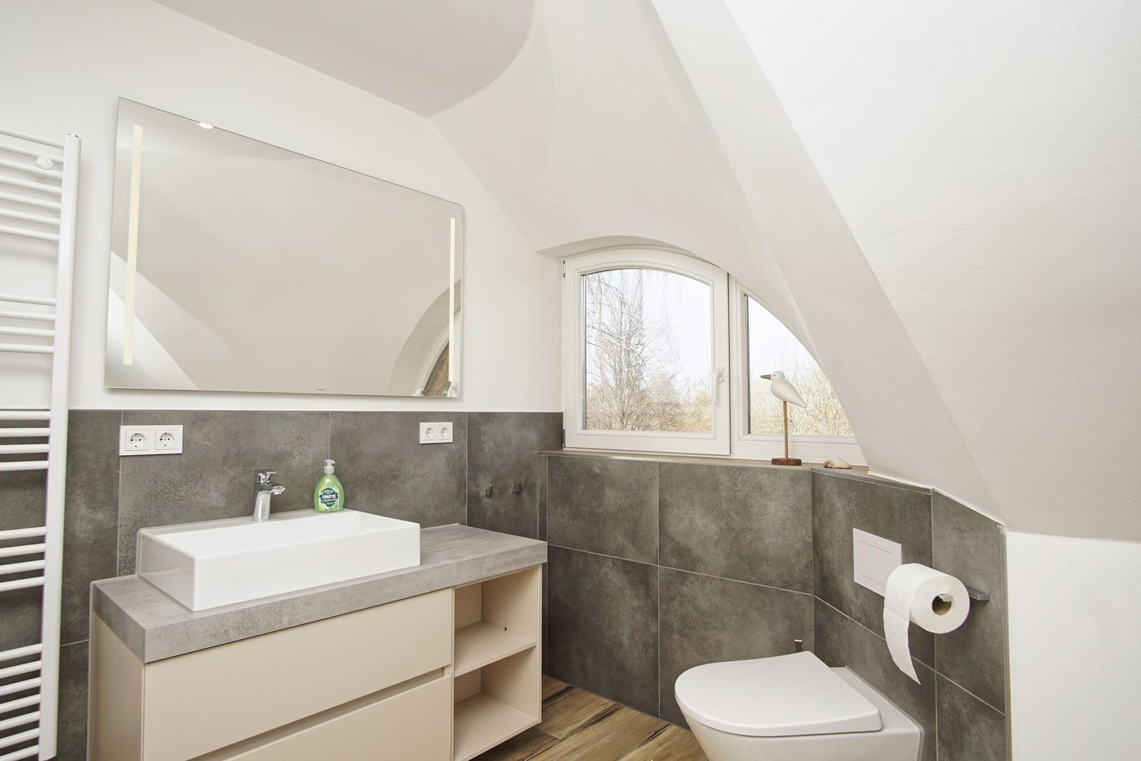 Badezimmer mit Waschtisch, Spiegel und Toilette unter Dachschrägen.