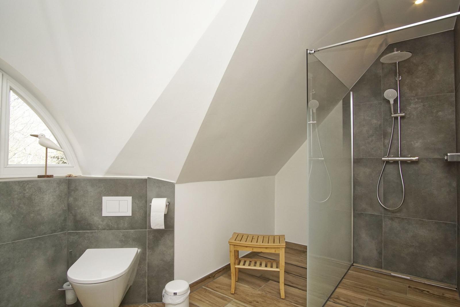 Badezimmer mit Dusche, WC und Holzbank unter Dachschrägen.
