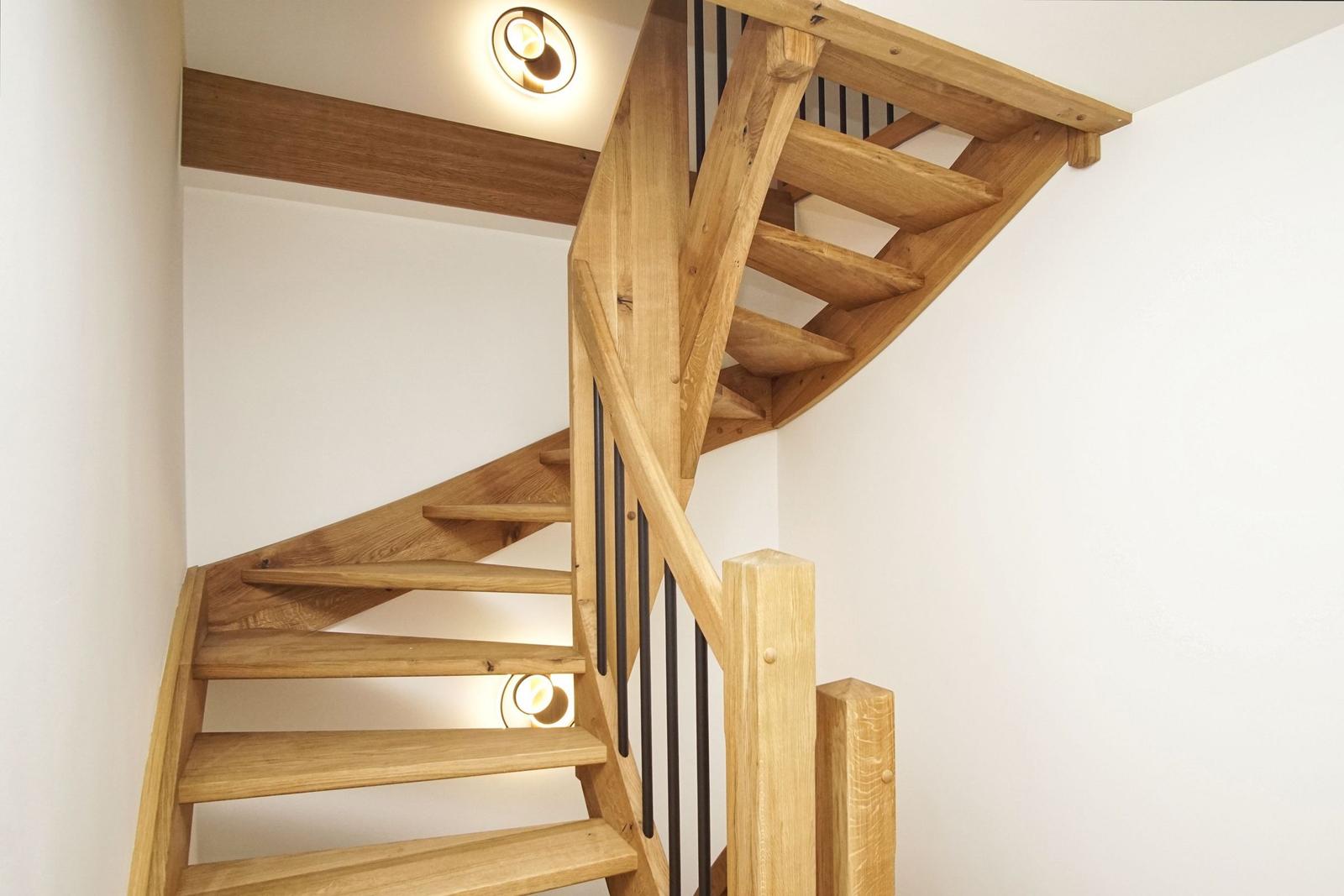 Holzgetreppe mit schwarzem Geländer und Deckenleuchte.