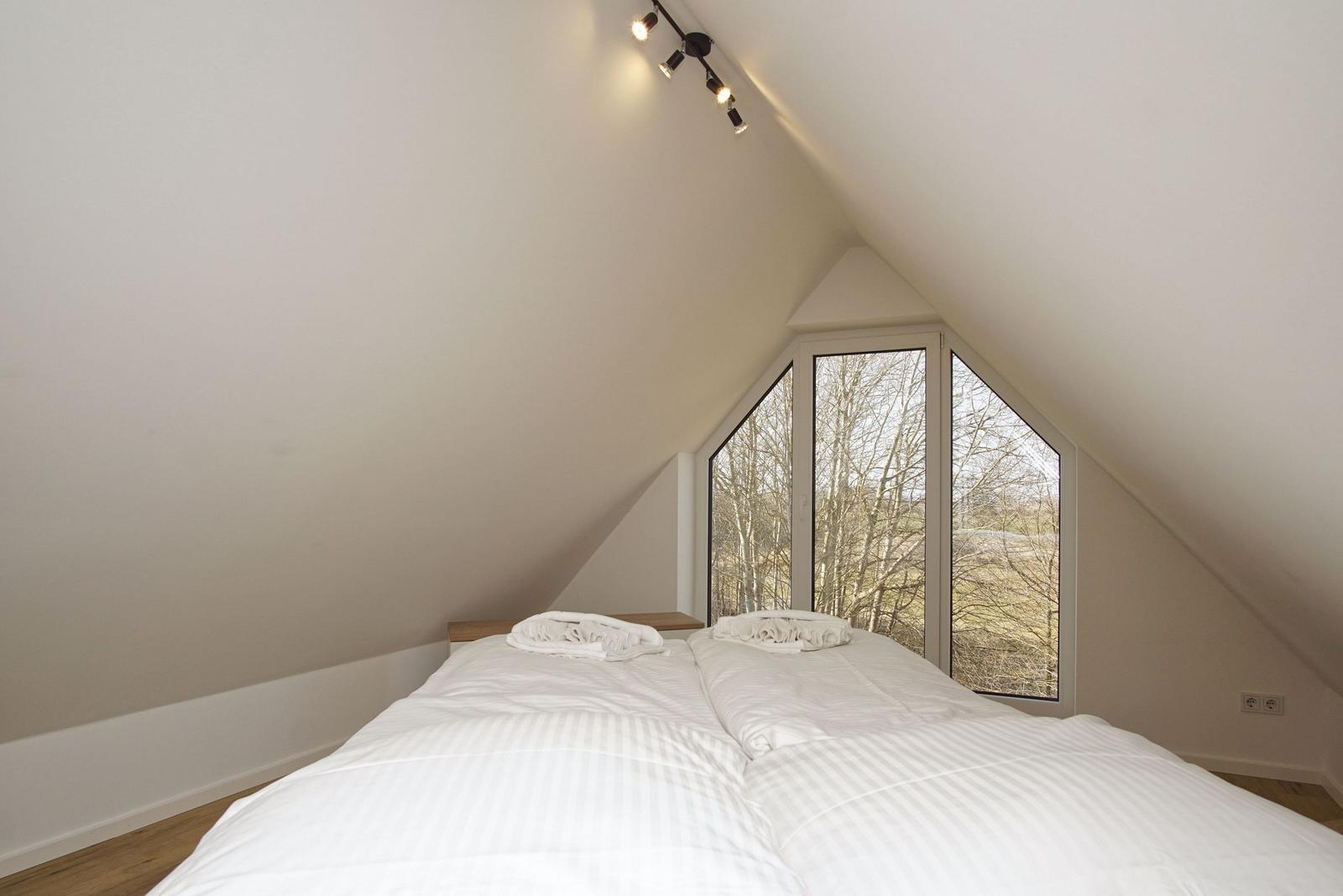 Schlafzimmer mit Doppelbett und großem Fenster zur Waldsicht.