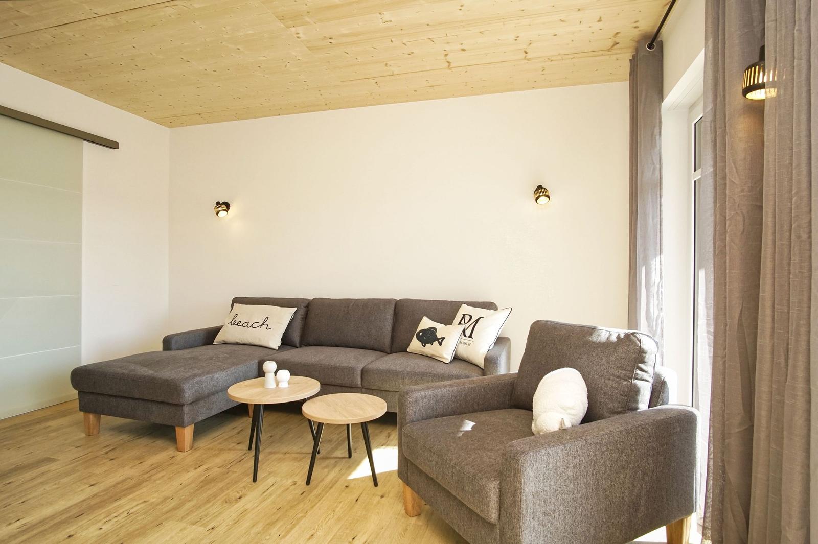 Wohnzimmer mit grauem Sofa, zwei runden Tischen und Holzboden.