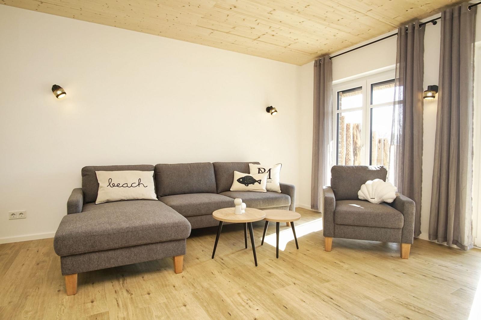 Wohnzimmer mit grauem Sofa, Sessel und Holzboden. An der Wand hängen zwei Lampen.