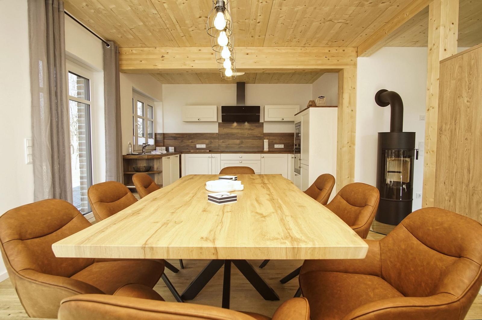 Esszimmer mit Holztisch und braunen Stühlen. Küchenbereich und Kamin im Hintergrund.
