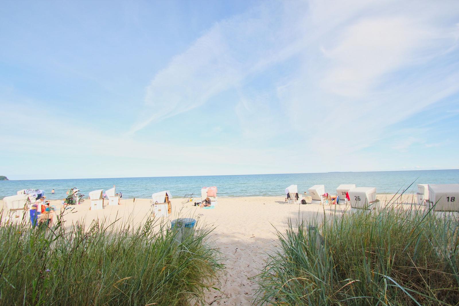 Strand mit weißen Strandkörben und Sanddünen im Vordergrund.