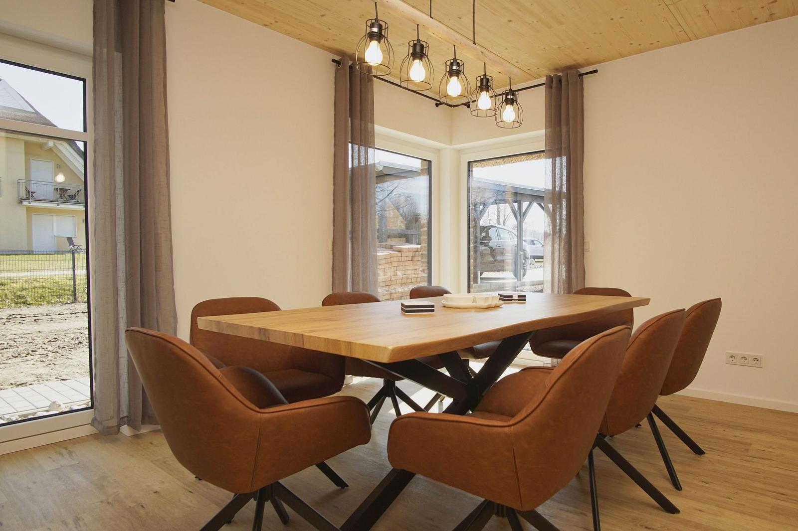 Esszimmer mit Holztisch, braunen Stühlen und großen Fenstern.