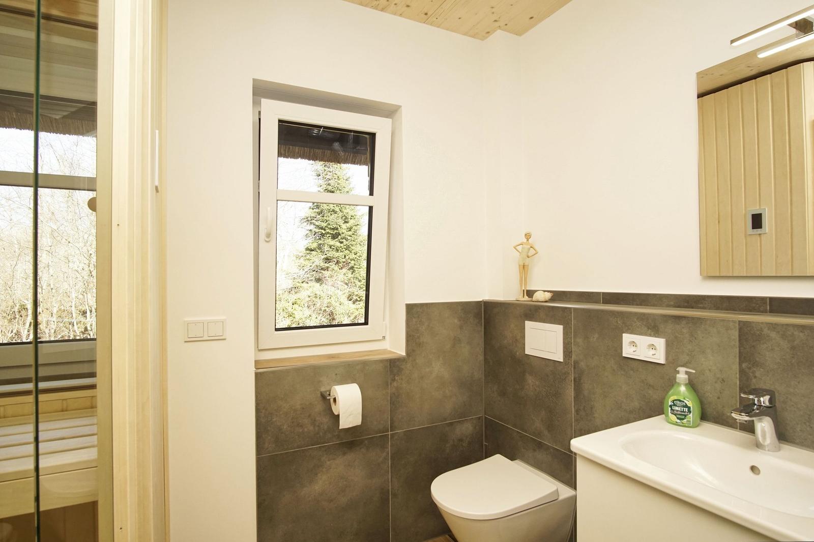 Badezimmer mit Toilette, Waschbecken und Fenster zur Waldansicht.