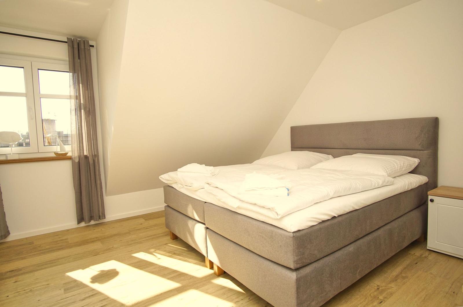 Schlafzimmer mit Doppelbett, Holzboden und Fenster mit Vorhängen.