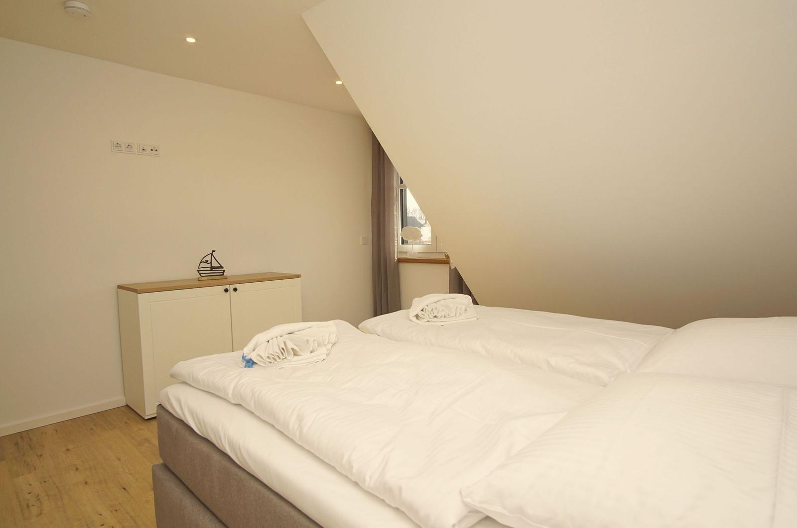 Schlafzimmer mit Doppelbett, Schrank und Fenster unter Dachschrägen.