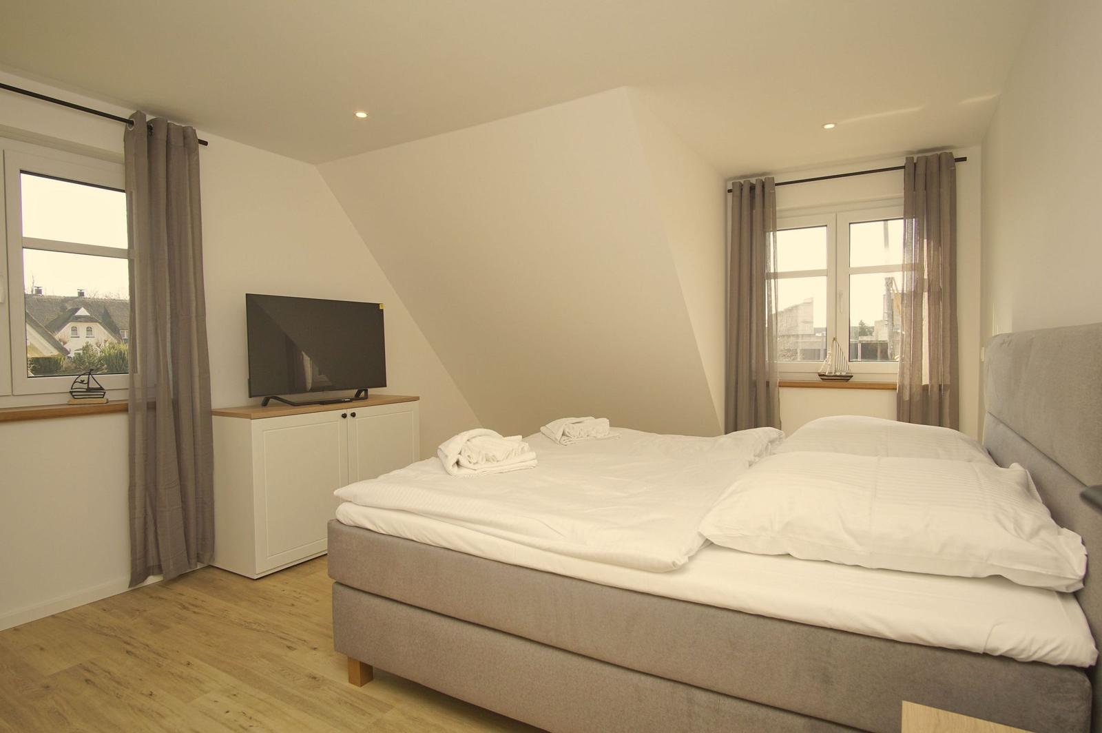 Schlafzimmer mit Doppelbett, TV und zwei Fenstern mit Blick.