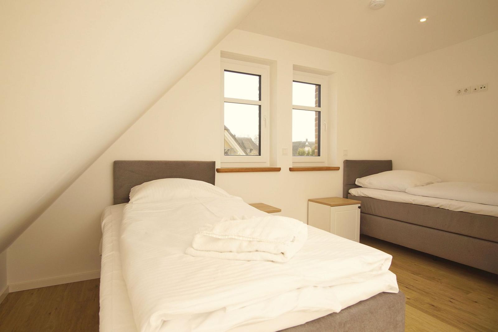 Zwei Betten in einem Dachgeschosszimmer mit Fenstern und Holzboden.