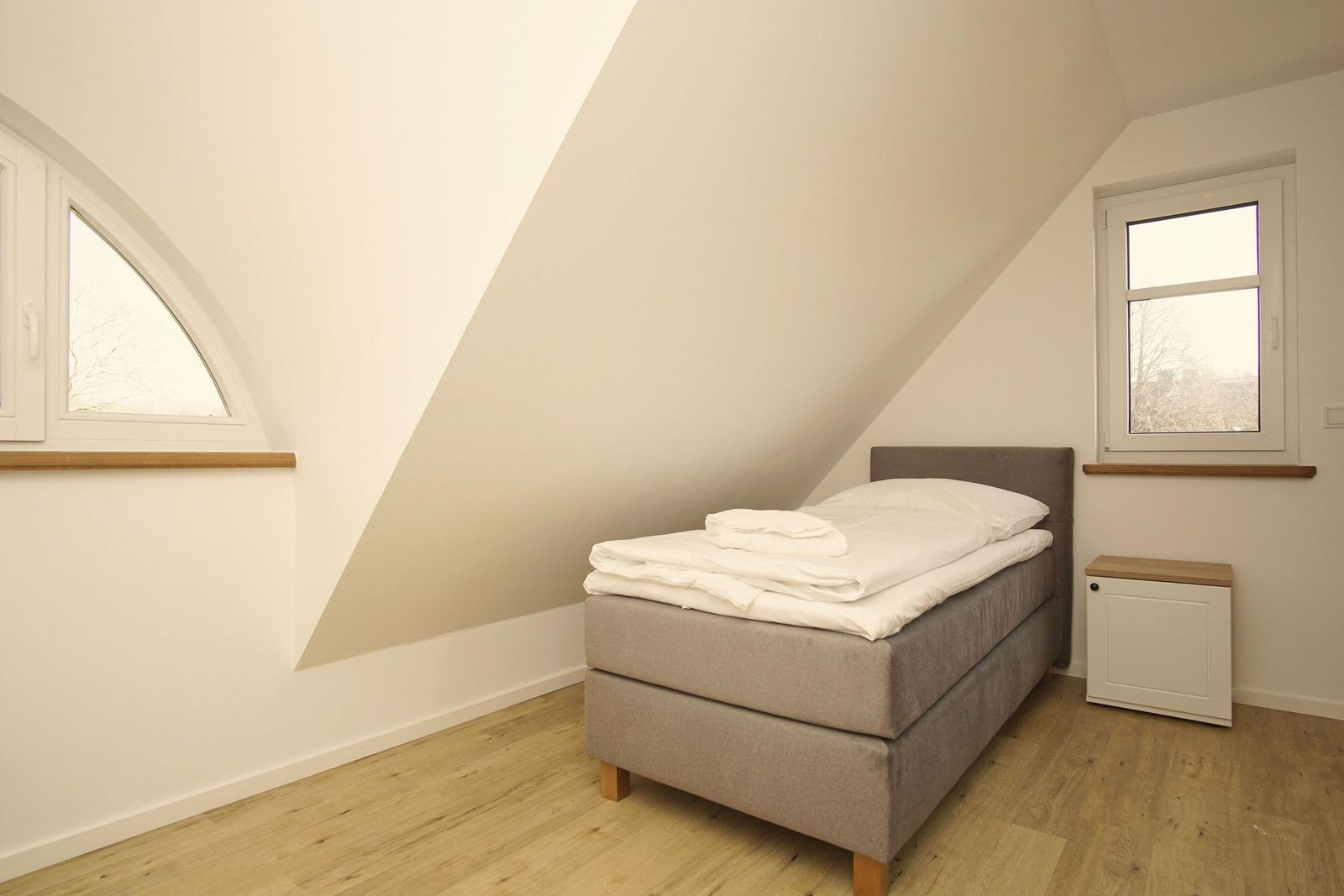 Schlafzimmer mit Dachschräge, Bett, Fenster und Holzboden.