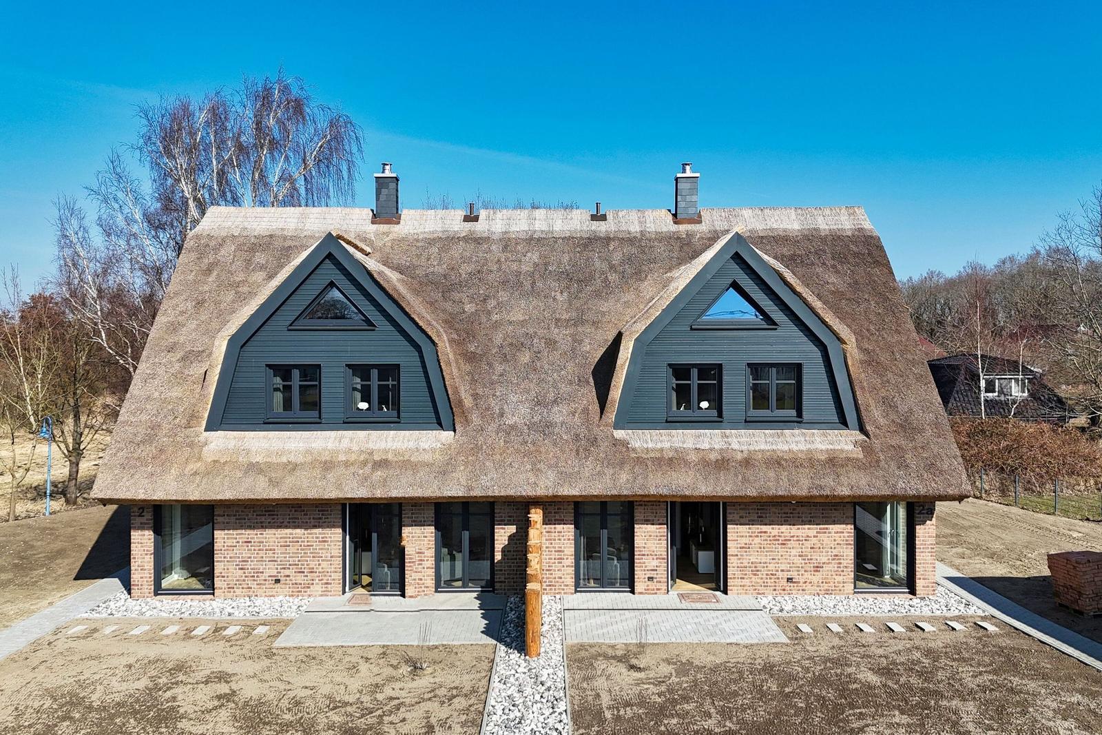 Moderne Villa mit strohgedecktem Dach und großen Fenstern.