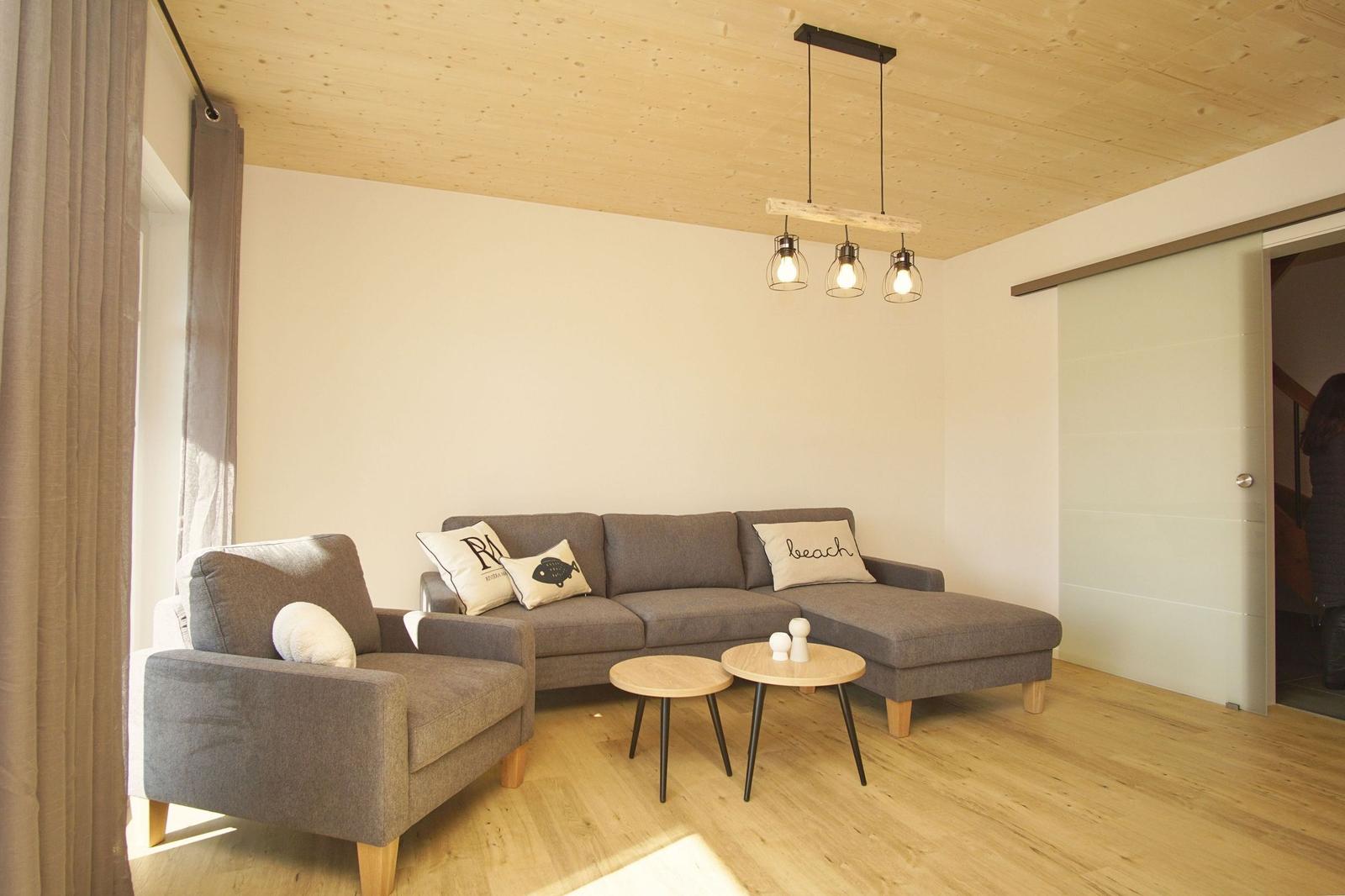 Wohnzimmer mit grauem Sofa, Holzdecke und zwei runden Tischen.