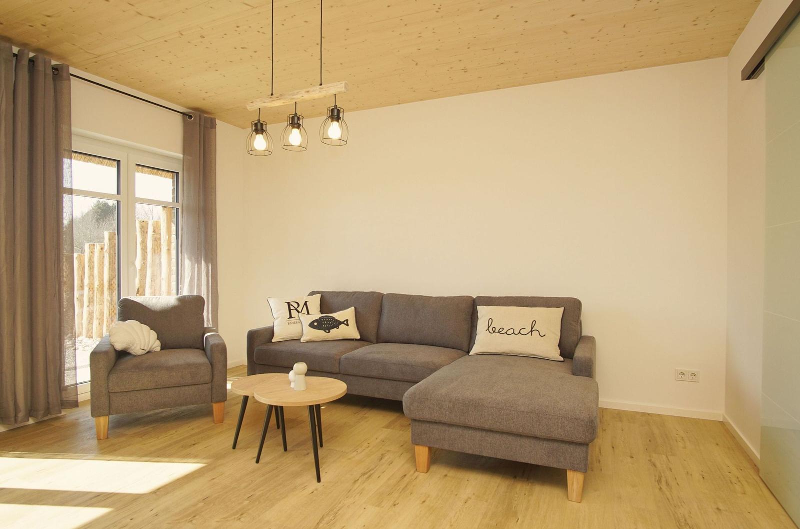 Wohnzimmer mit grauem Sofa, Tisch und Fenster. Holzdecke und Boden.