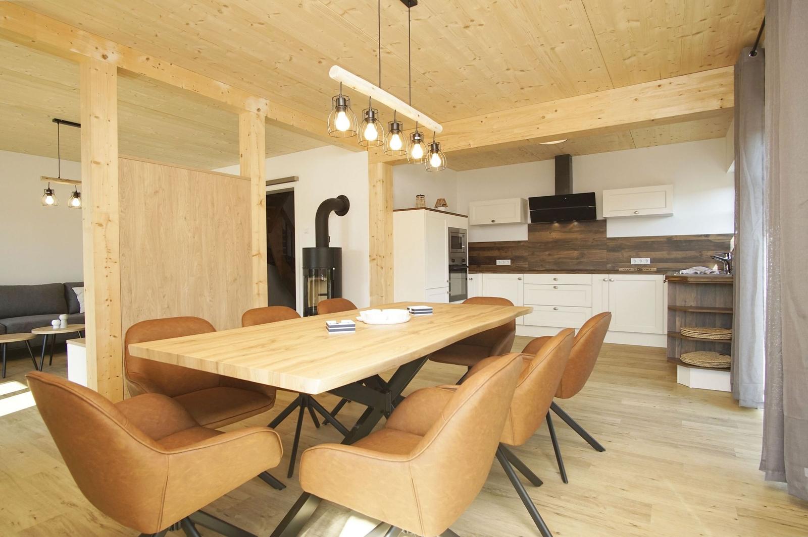 Essbereich mit Holztisch und Ledersitzen, Küche im Hintergrund, Holzdecke und -boden.
