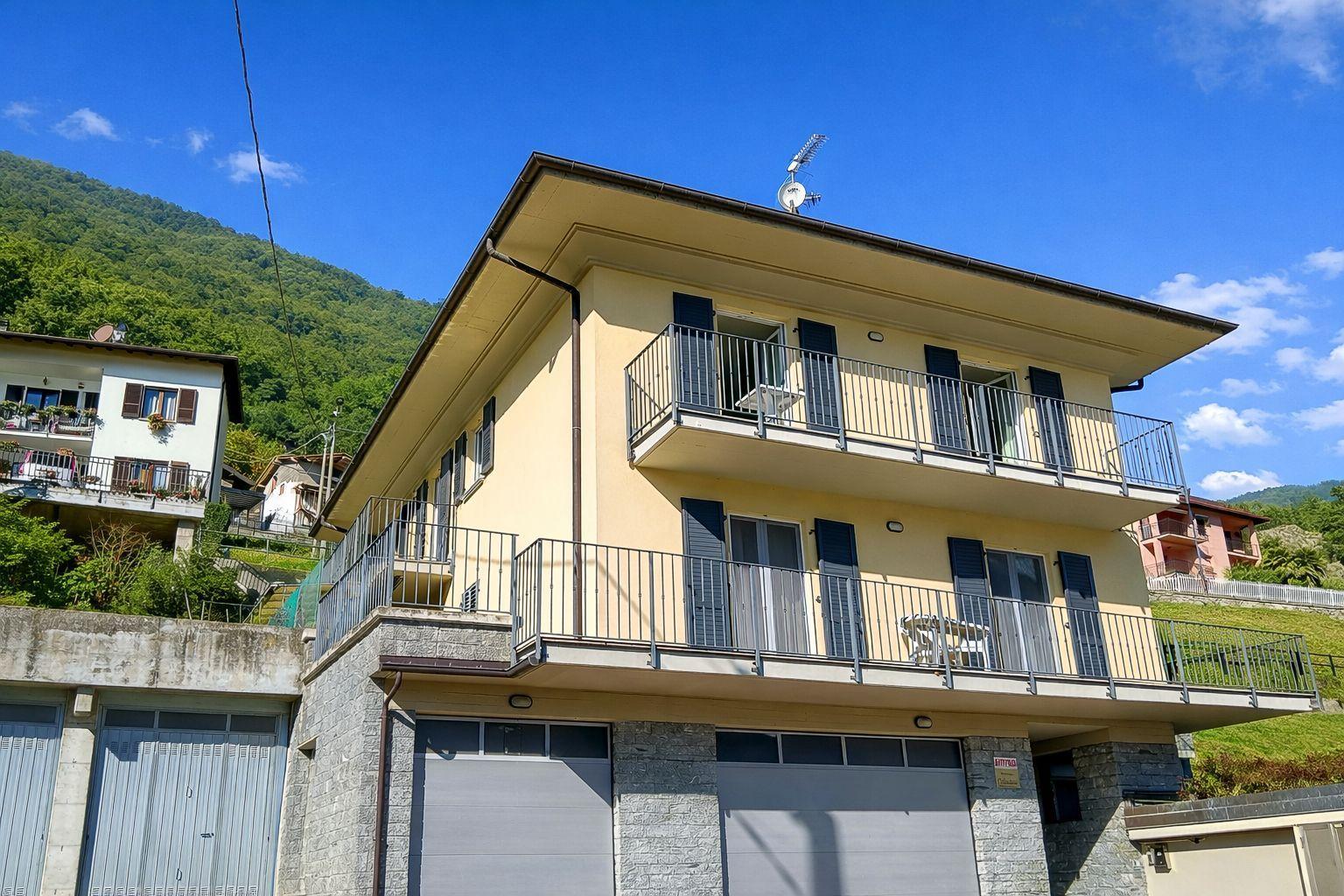 Zweistöckiges Haus mit Balkonen und Garage. Berglandschaft im Hintergrund.