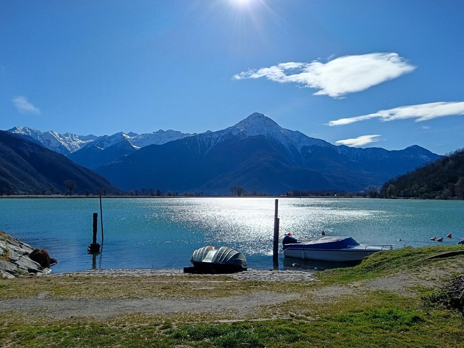 Lakeside with boats and snow-capped mountains under clear blue sky.
