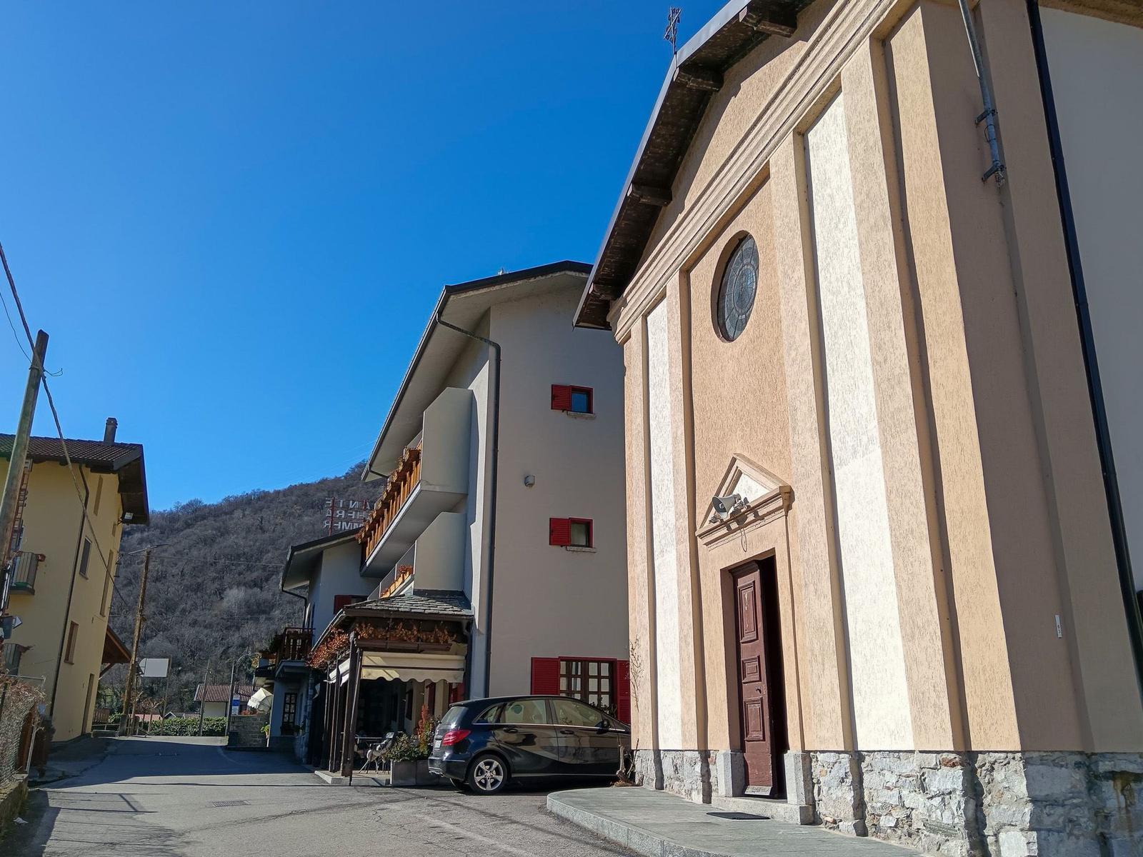 Kirche mit runder Fensteröffnung und Holztür. Autos parken vor dem Gebäude.