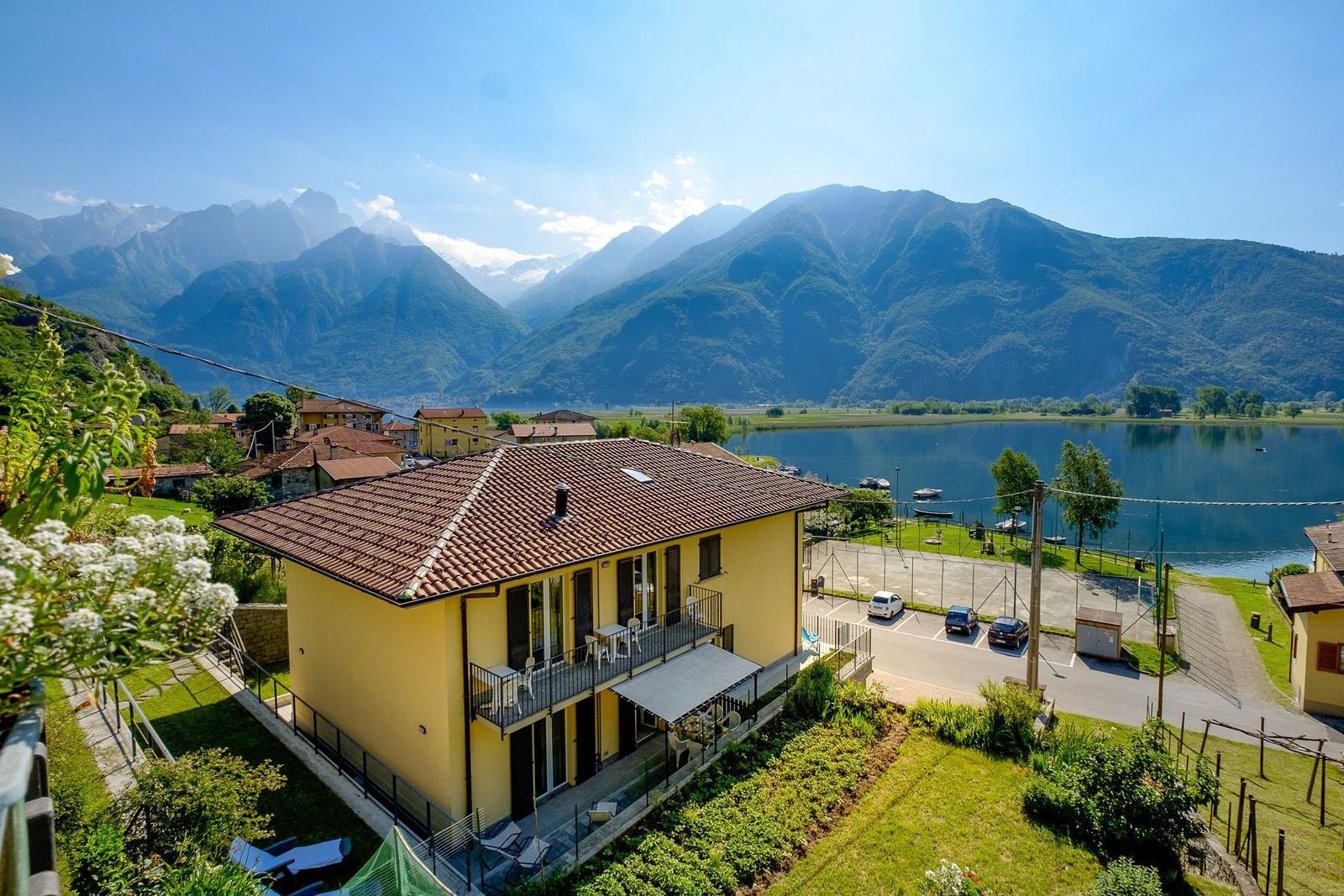 Gelbes Haus mit Balkon, See und Bergen im Hintergrund.