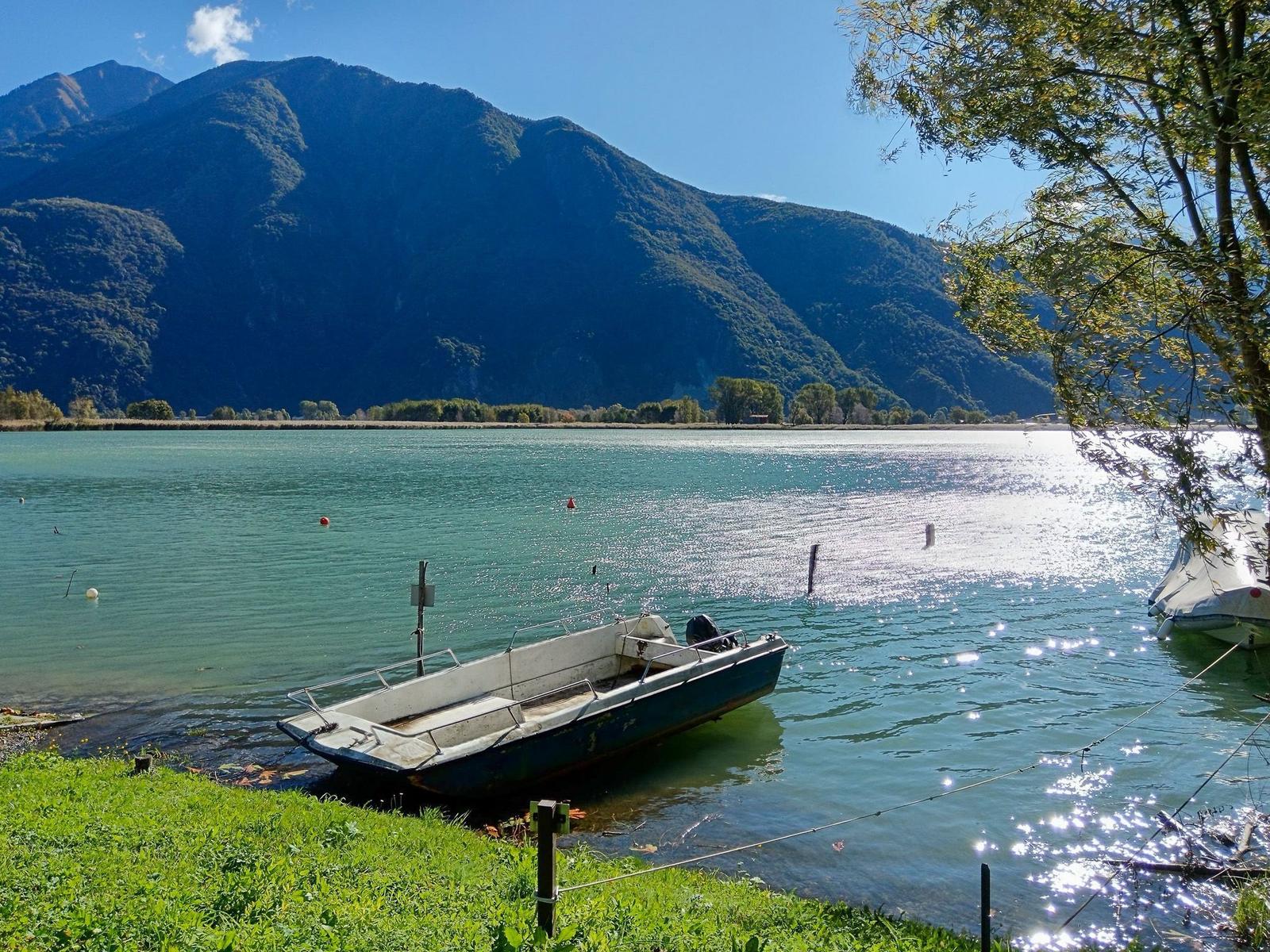 Ein kleines Boot liegt am Ufer eines Sees mit Bergen im Hintergrund.