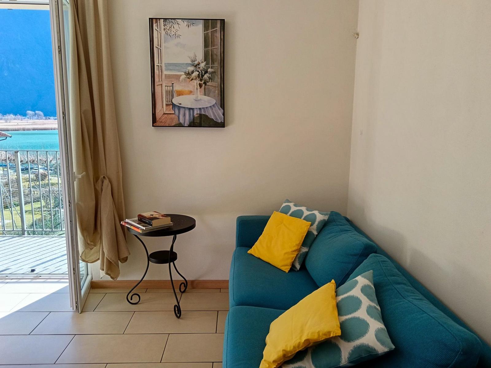 Ein Wohnbereich mit blauem Sofa, Kissen und einem Tisch neben einer Balkontür.