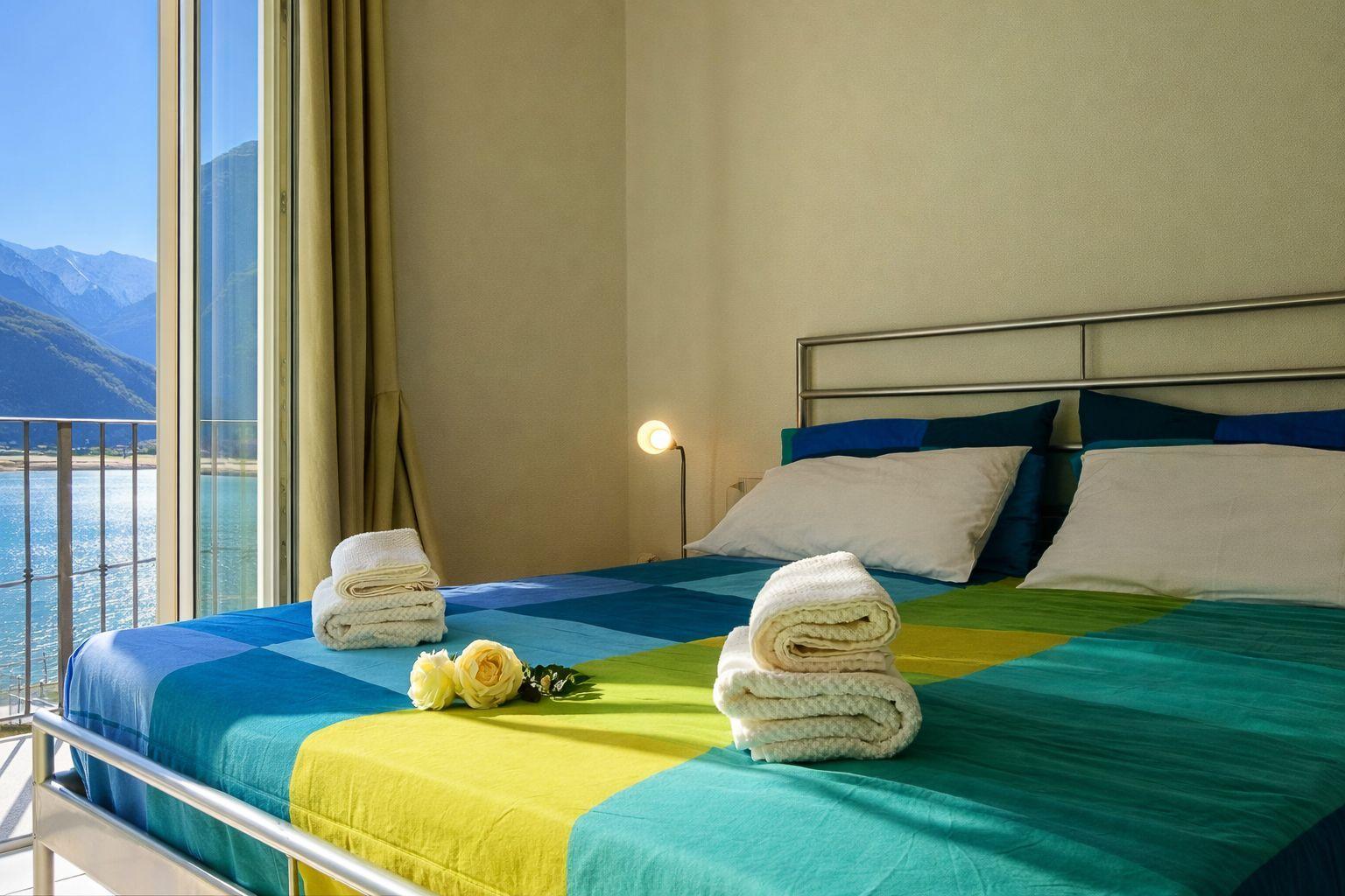 Schlafzimmer mit Blick auf See und Berge. Bett mit bunten Laken und Handtüchern.