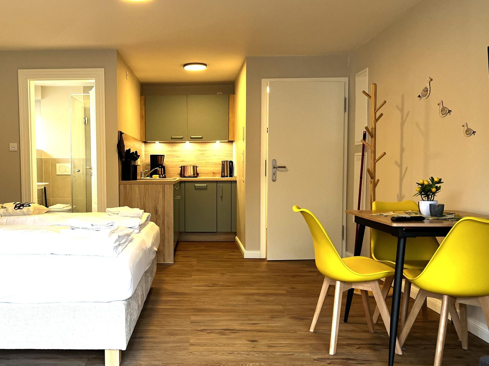 Schlafzimmer mit kleiner Küche und Essbereich mit gelben Stühlen.