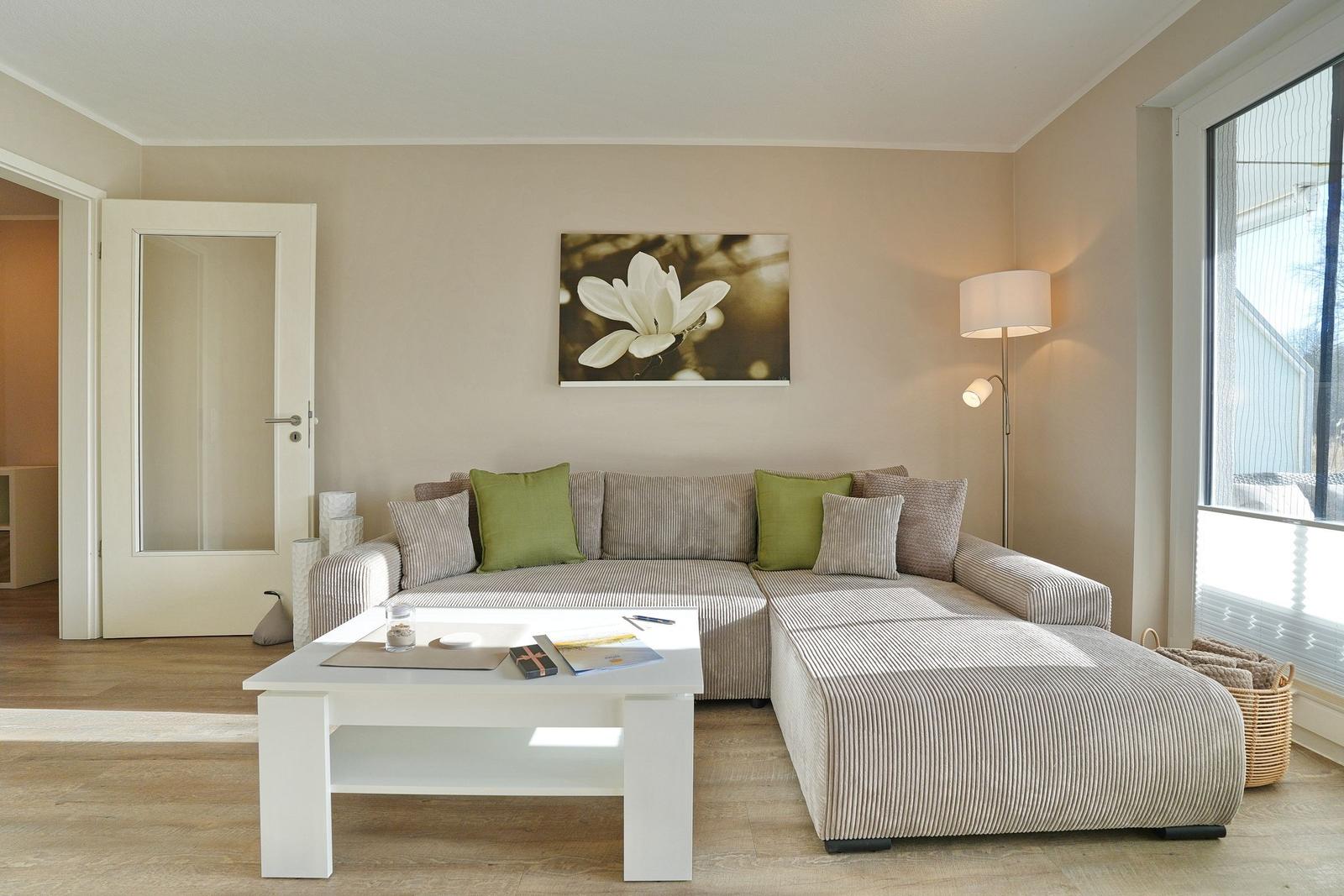 Wohnzimmer mit Ecksofa, Tisch und Wandbild. Tür und Fenster sichtbar.