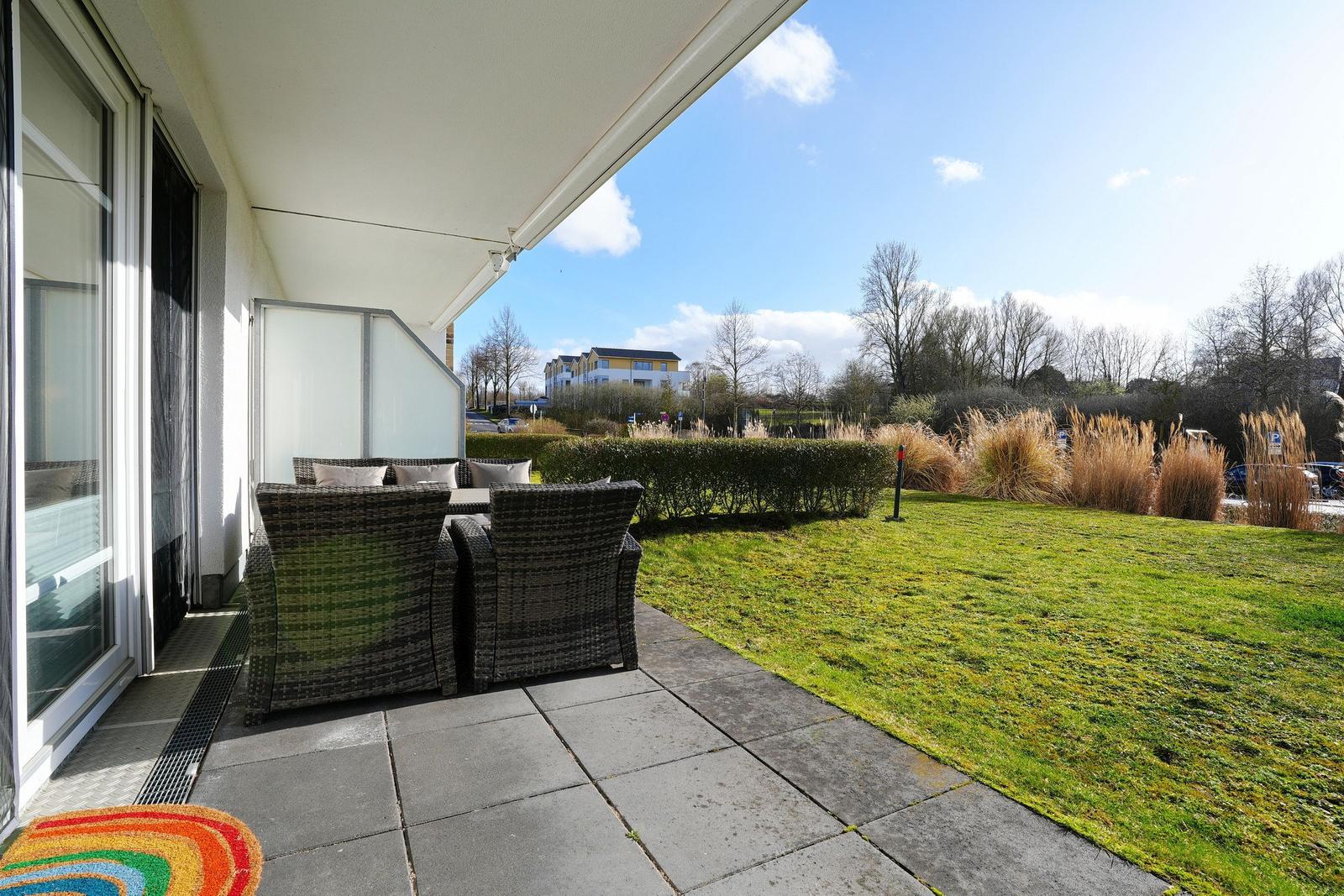 Terrasse mit Sitzgruppe, Rasen und Blick auf Bäume.